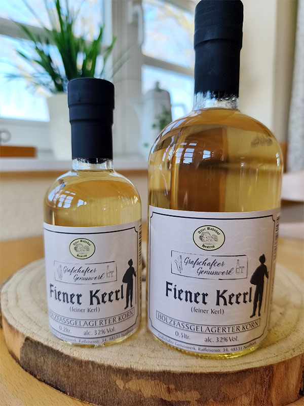 Zwei Flaschen Fiener Keerl holzfassgelagerter Korn vom Grafschafter Genusswerk in den Größen 0,2 Liter und 0,5 Liter auf einer Holzscheibe.