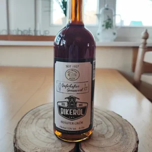 Eine 0,5-Liter-Glasflasche mit dunklem Kräuterlikör namens „Bikeröl“, stehend auf einer rustikalen Holzscheibe. Das Etikett zeigt eine Motorrad-Illustration und den Schriftzug „Grafschafter Genusswerk“.